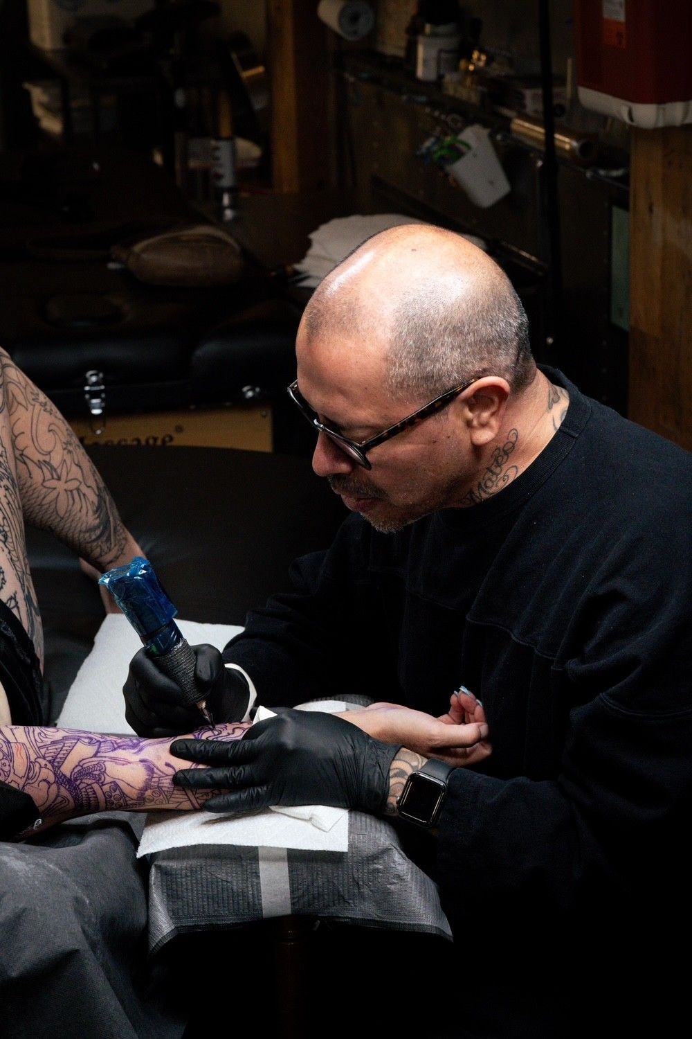 Tattoo artist in black gloves working on a client’s tattoo in a dim studio