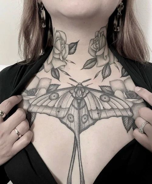 Close-up of a person showing floral neck and moth chest tattoos on a black top