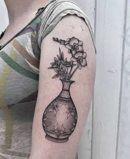 Arm tattoo of a vase with flowers in black linework on a shoulder, with a geometric sunburst inside the vase.