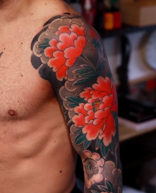 Close-up of a tattooed upper arm with red peony flowers and dark green leaves