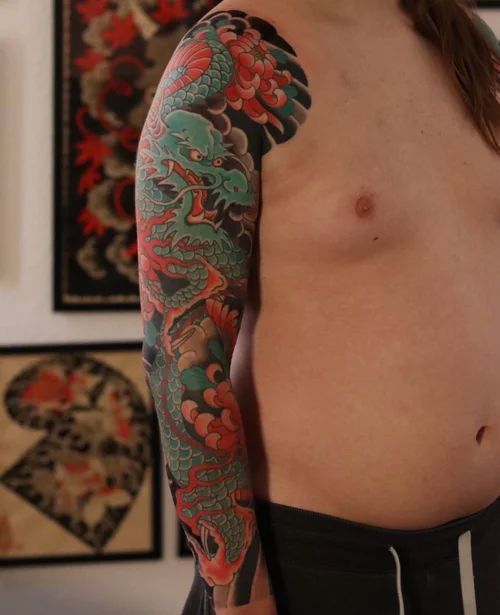 Torso and arm with a colorful dragon tattoo sleeve in a room with framed artwork.