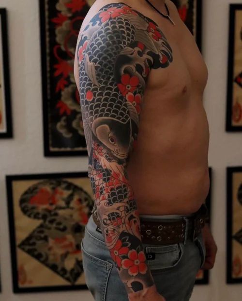 Side view of a shirtless torso with a colorful koi fish tattoo on the arm, standing indoors