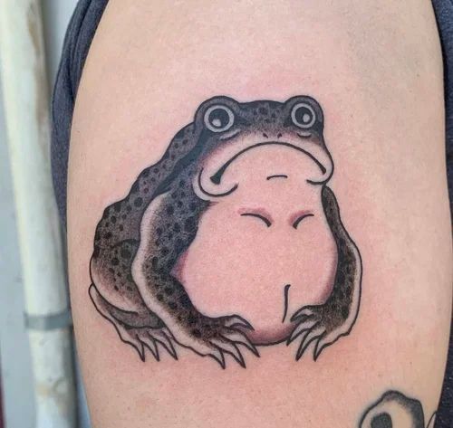 Small black-and-pink frog tattoo with closed eyes on skin
