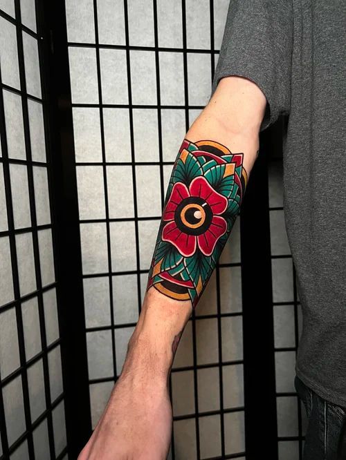 Arm with a colorful floral tattoo sleeve in red, green, and gold against a black grid backdrop