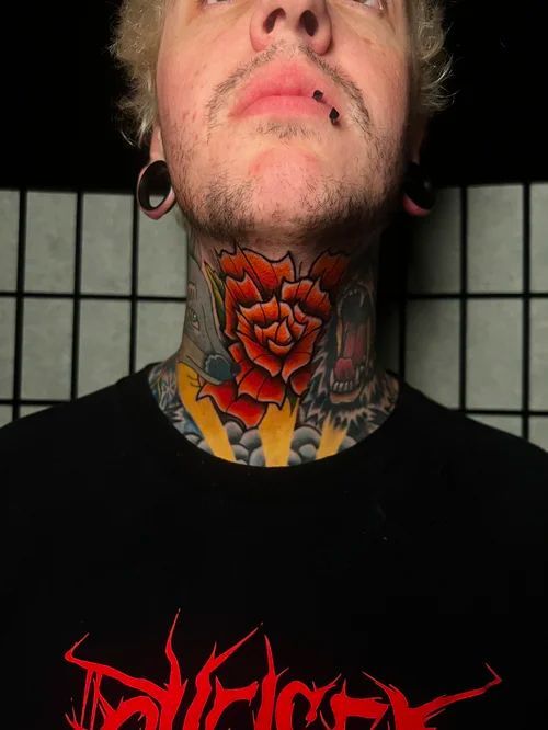 Person with tattoos and piercings wearing a black shirt, looking upward against a tiled background.