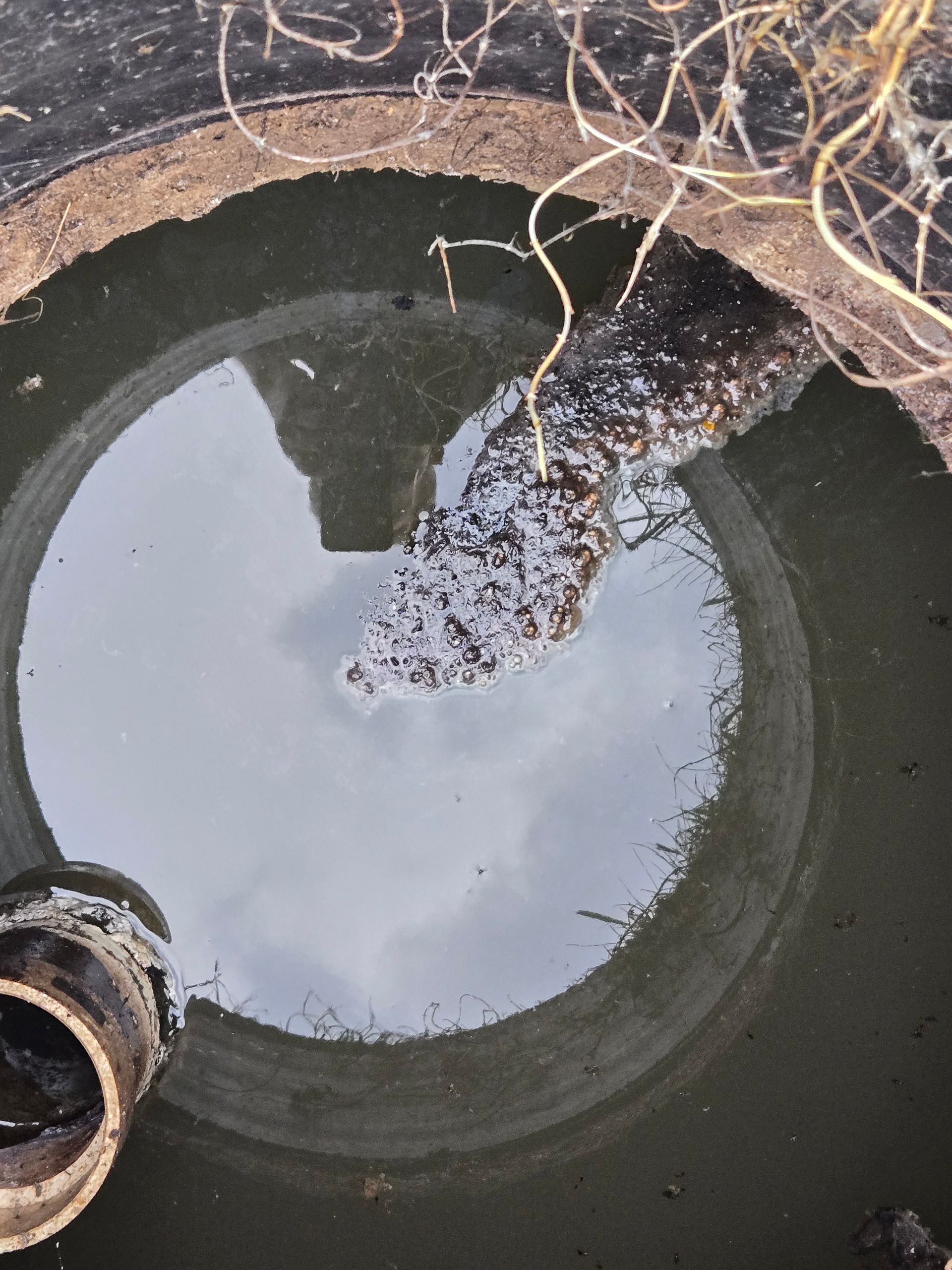 Water-filled round concrete tank with debris and a pipe opening on the left