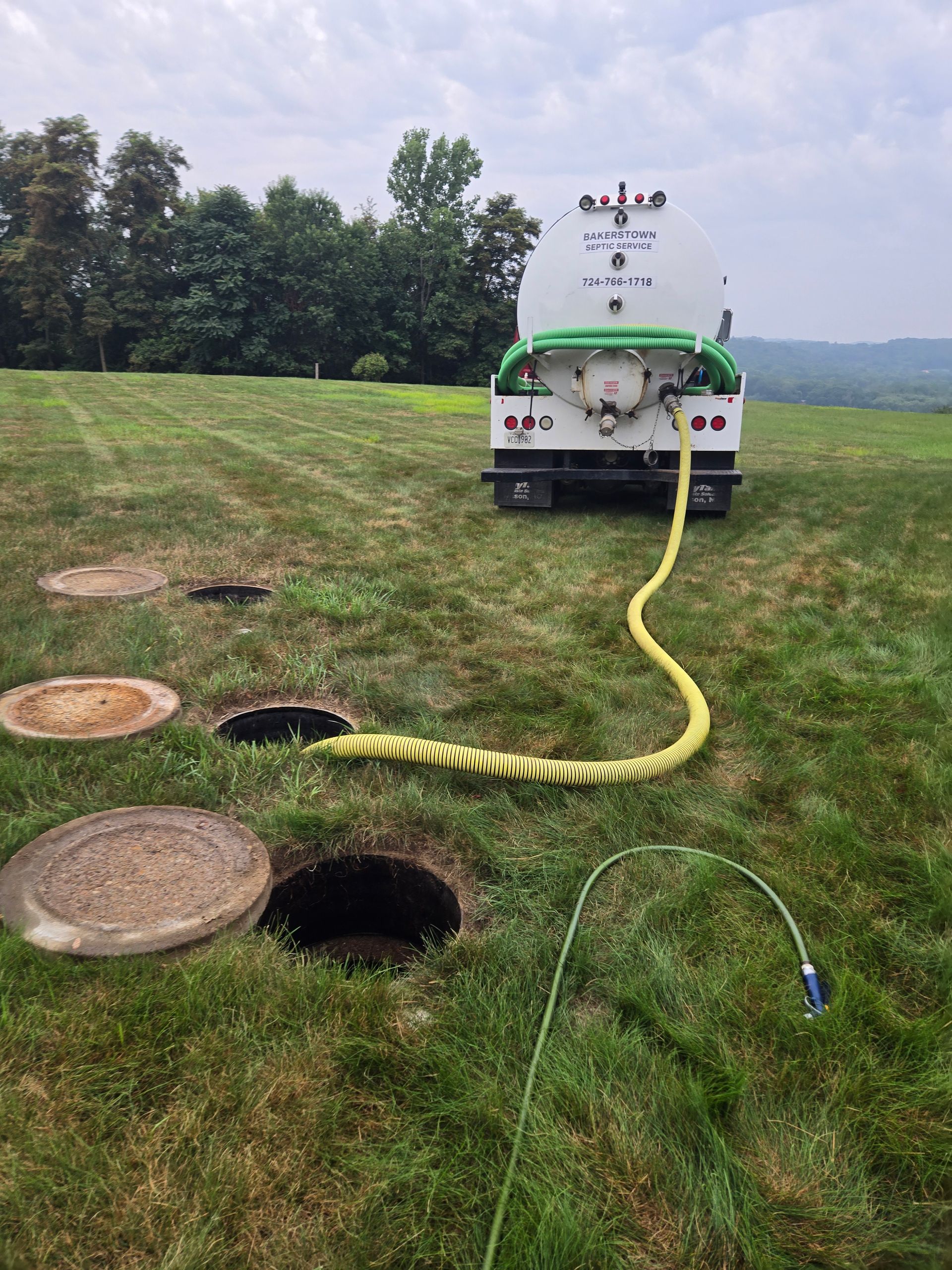 Utility truck pumping from an open manhole in a grassy field, with a yellow hose and exposed cable.