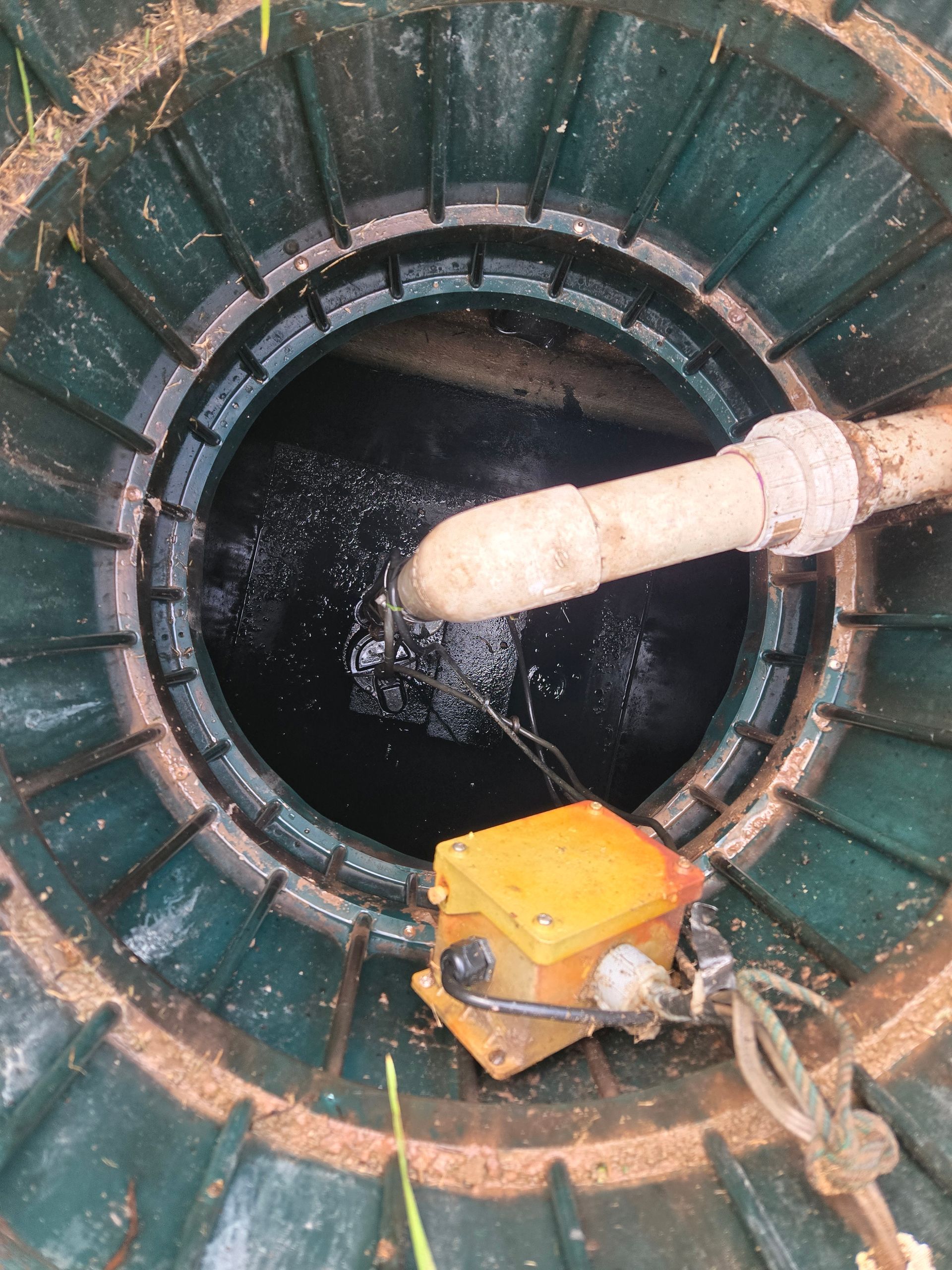 Pipe pouring water into a green circular well or tank, with a yellow pump at the edge