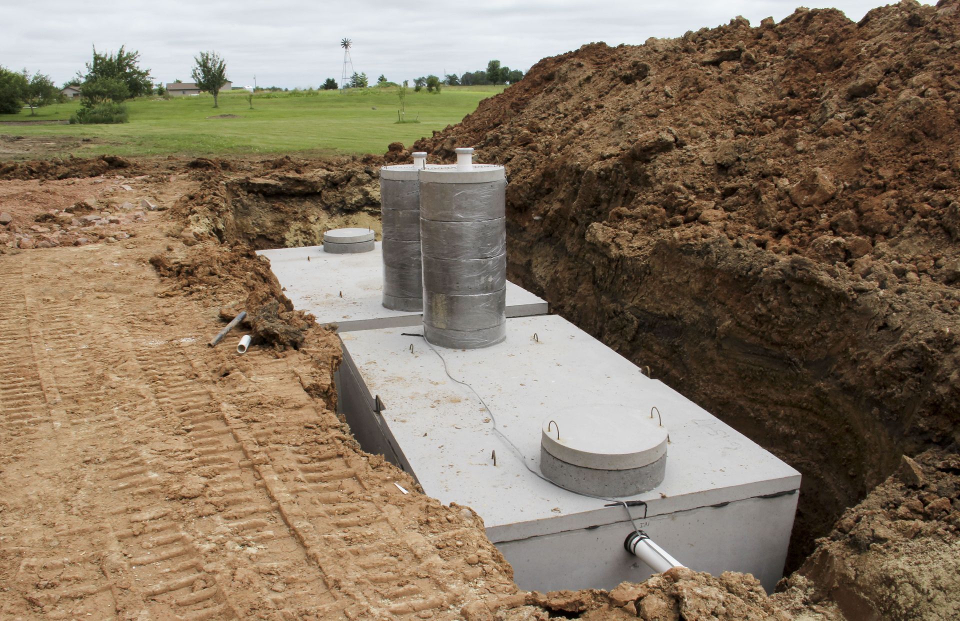 Concrete septic tank installed in an open trench beside a dirt mound on a grassy site