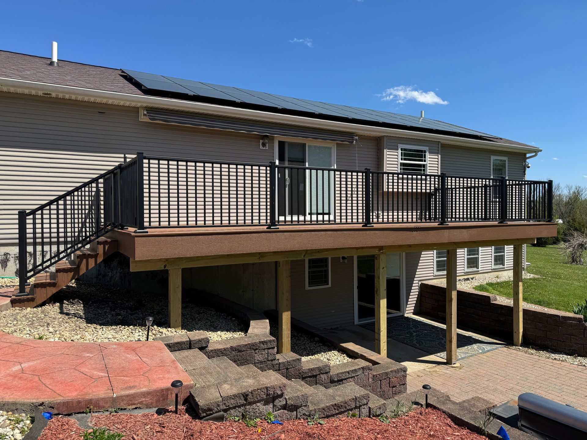 The back of a house with a large deck, railings, and stairs.
