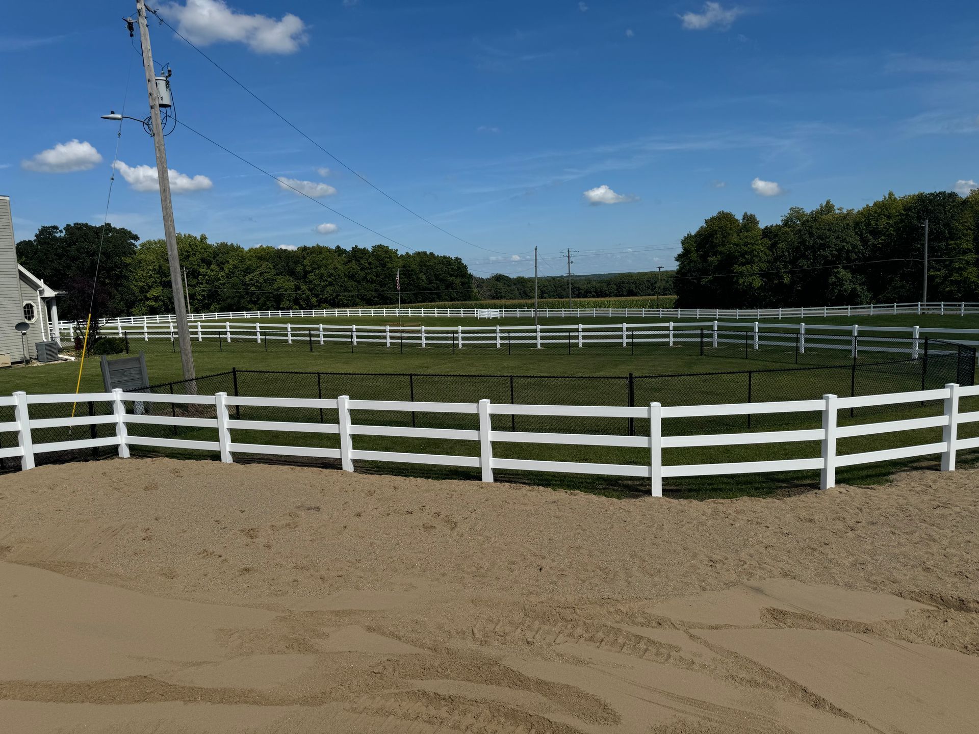 A white fence surrounds a dirt field with trees in the background.