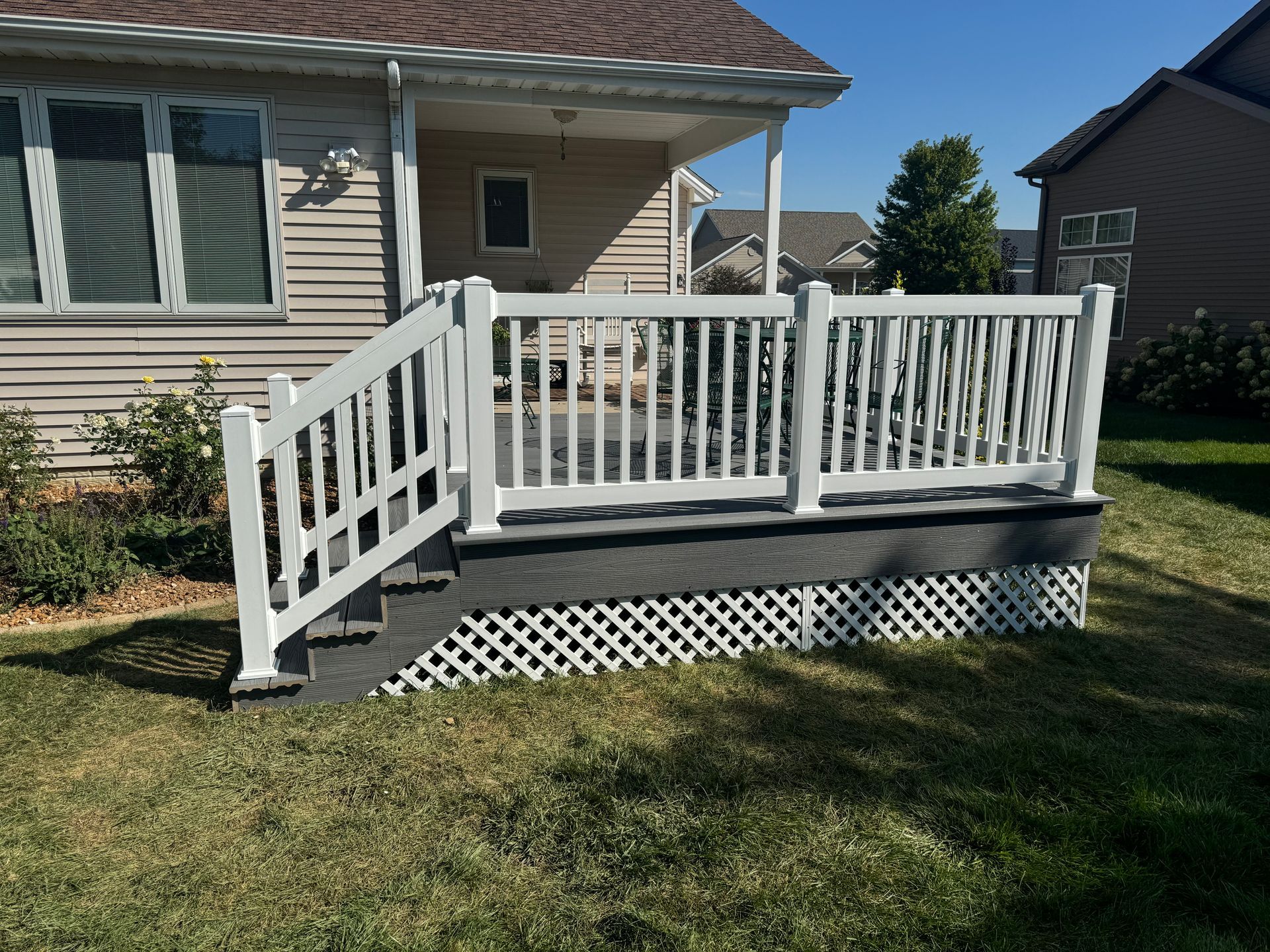 A white deck and railings with stairs leading up to it, are in front of a house.