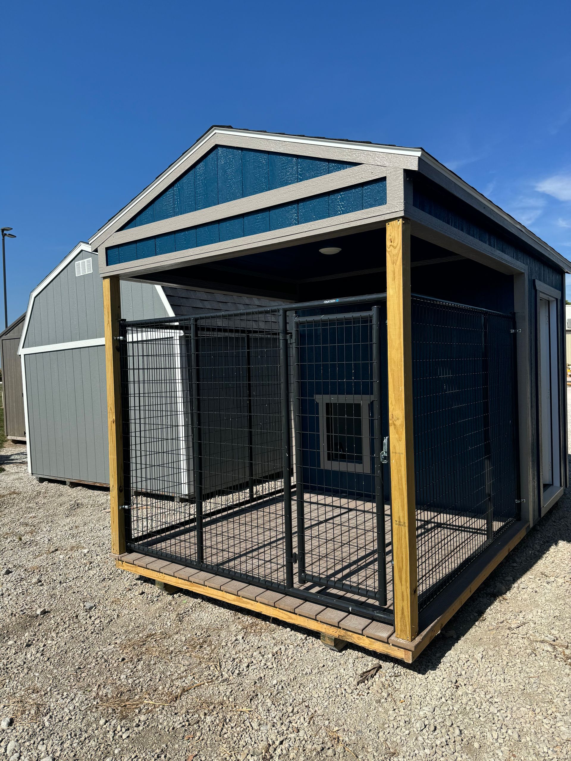 A dog kennel is sitting on top of a gravel lot.