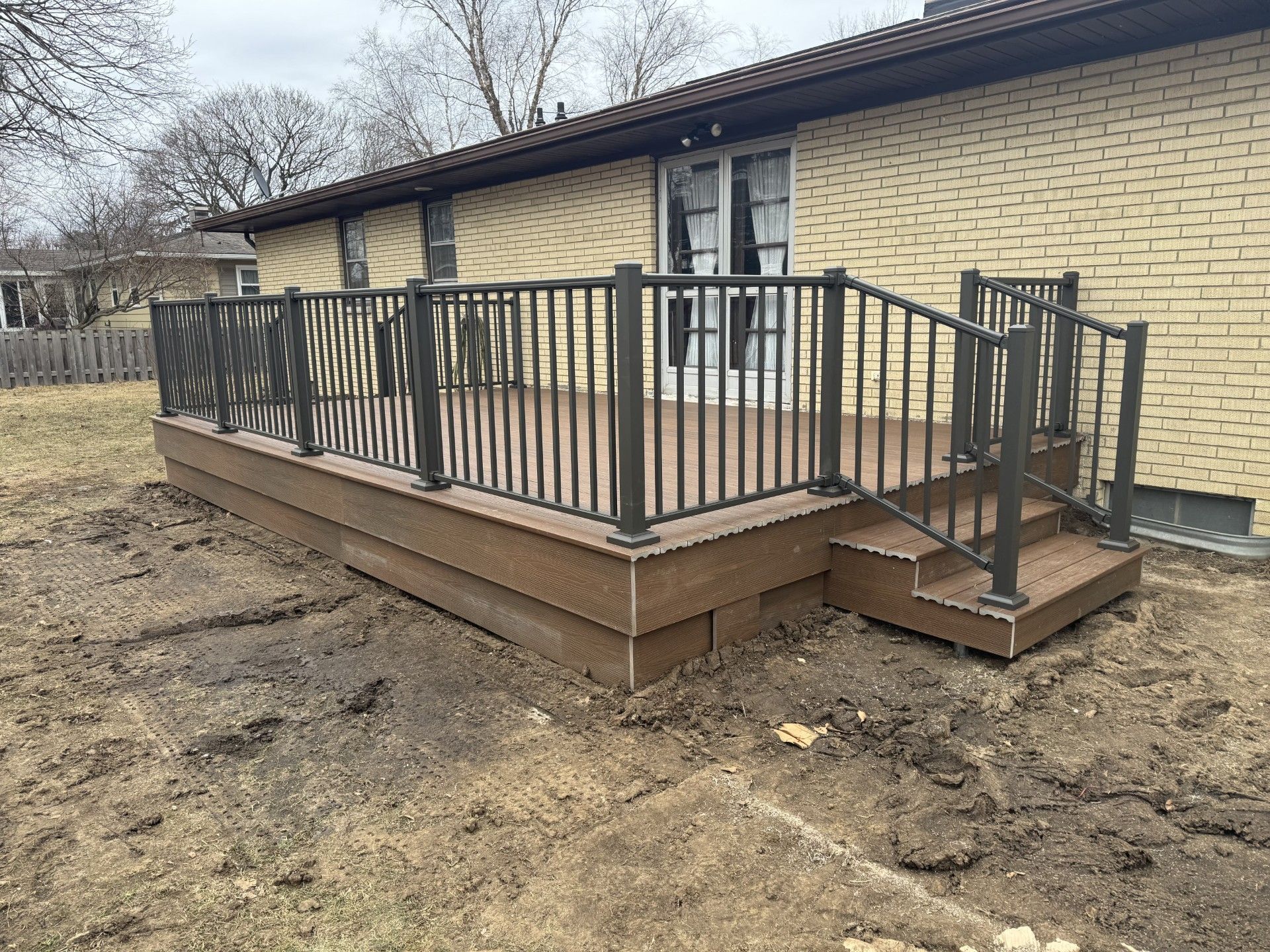 A deck with stairs and a railing in front of a brick house.