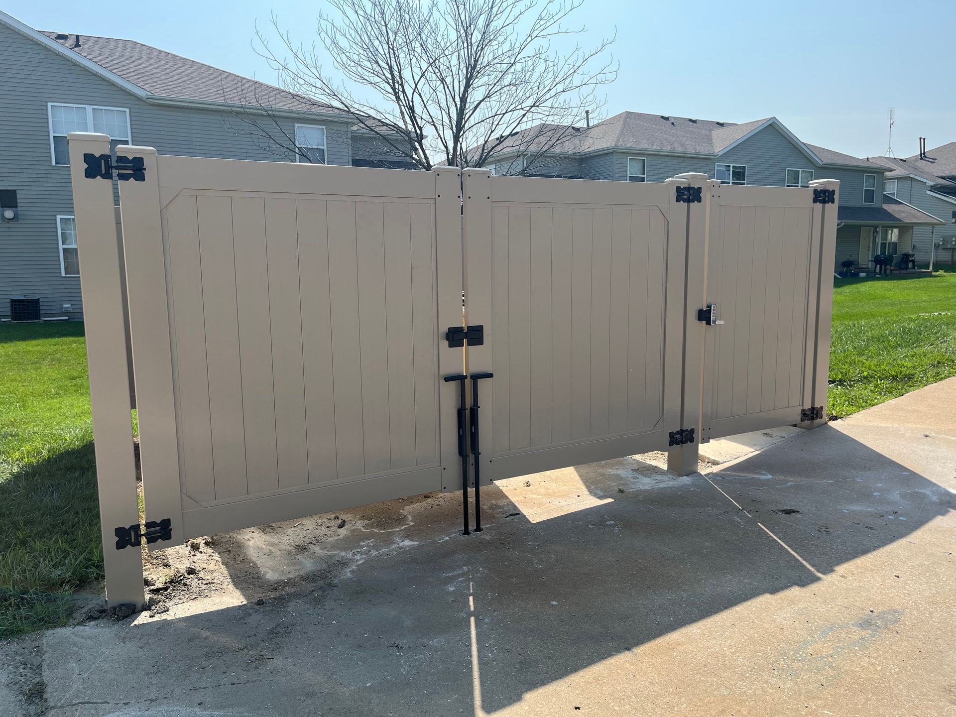 A beige fence is sitting on the side of a road in front of a house.
