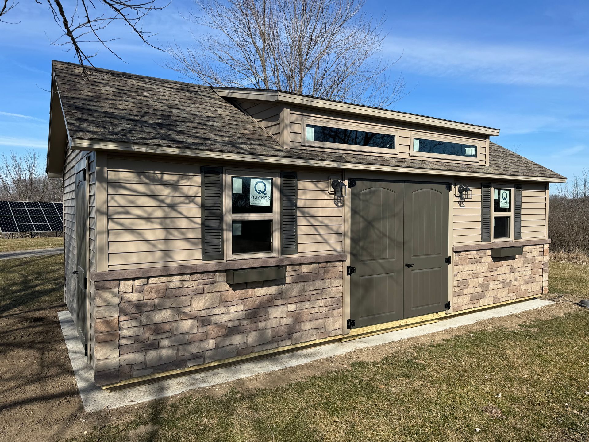 A small shed with a roof and windows is sitting in the middle of a grassy field.