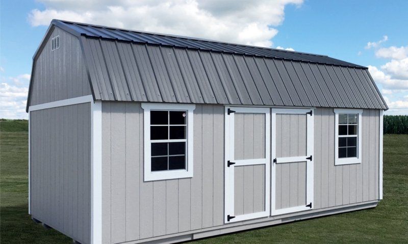 A shed with a gray roof and white trim is sitting on top of a lush green field.