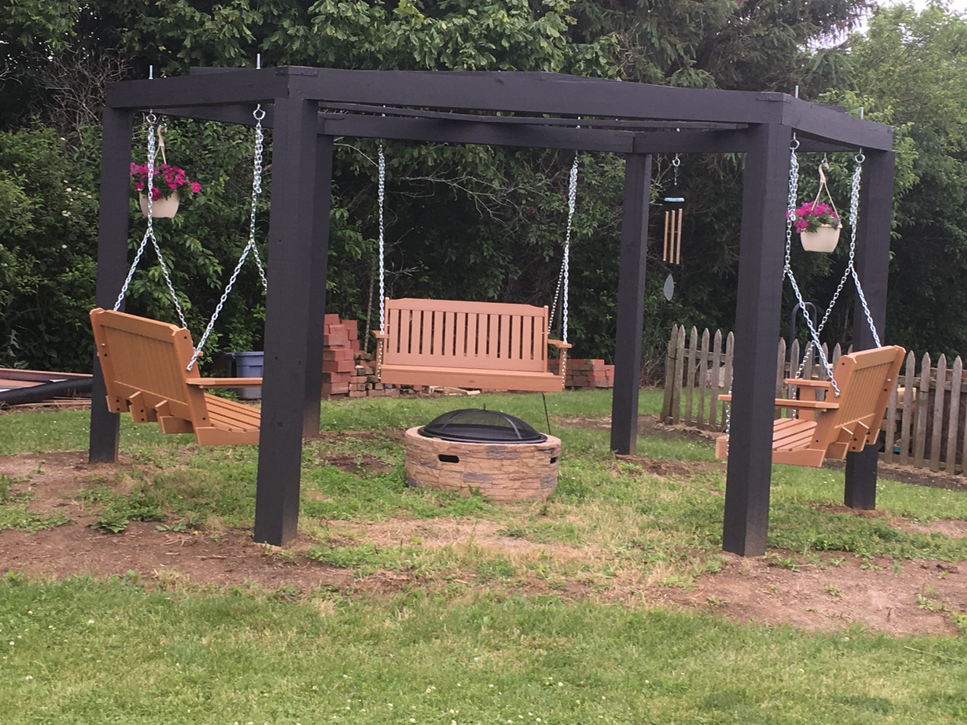 A wooden swing set in a backyard with a fire pit in the middle.