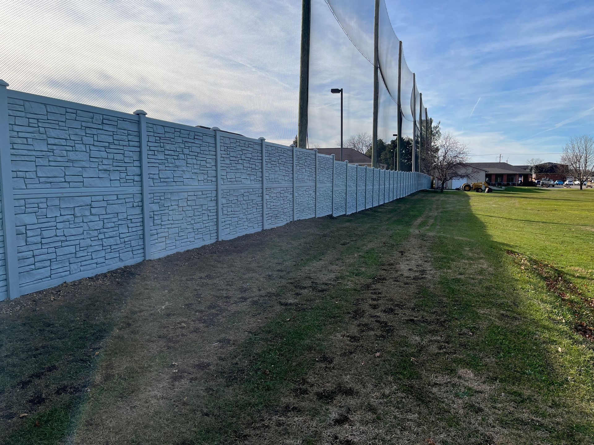 A white fence surrounds a grassy field in a park.