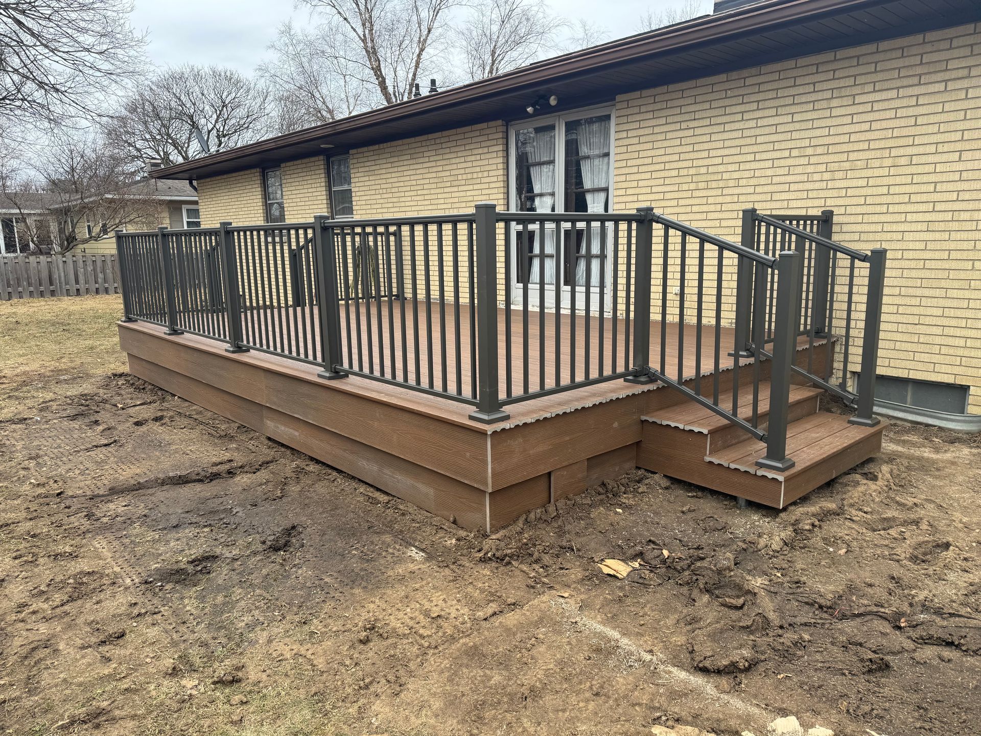 A deck with stairs and a railing in front of a brick house.