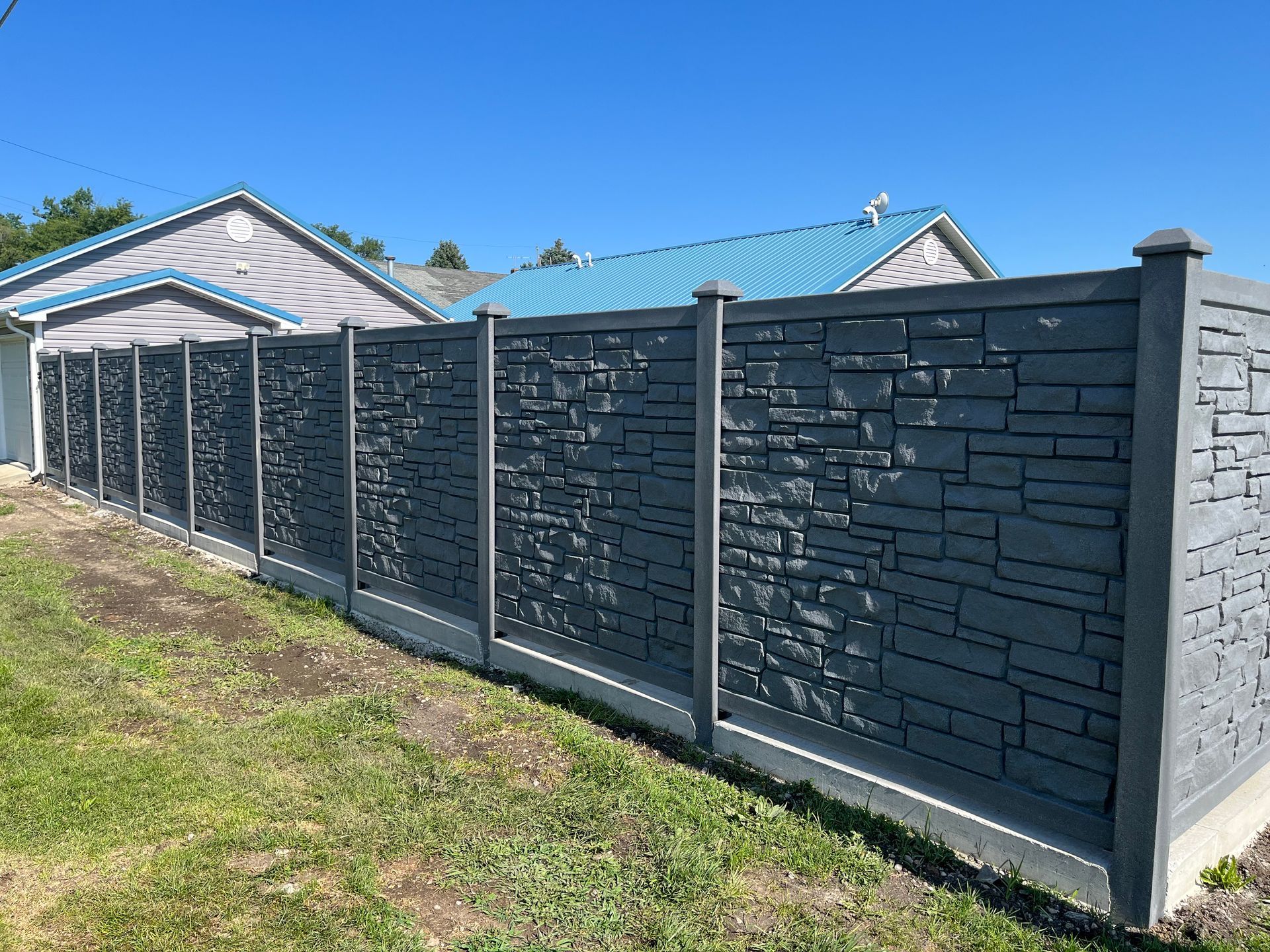 A concrete fence is sitting in the grass in front of a house.