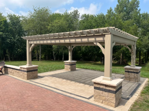 A pergola is sitting on top of a brick patio in a park.