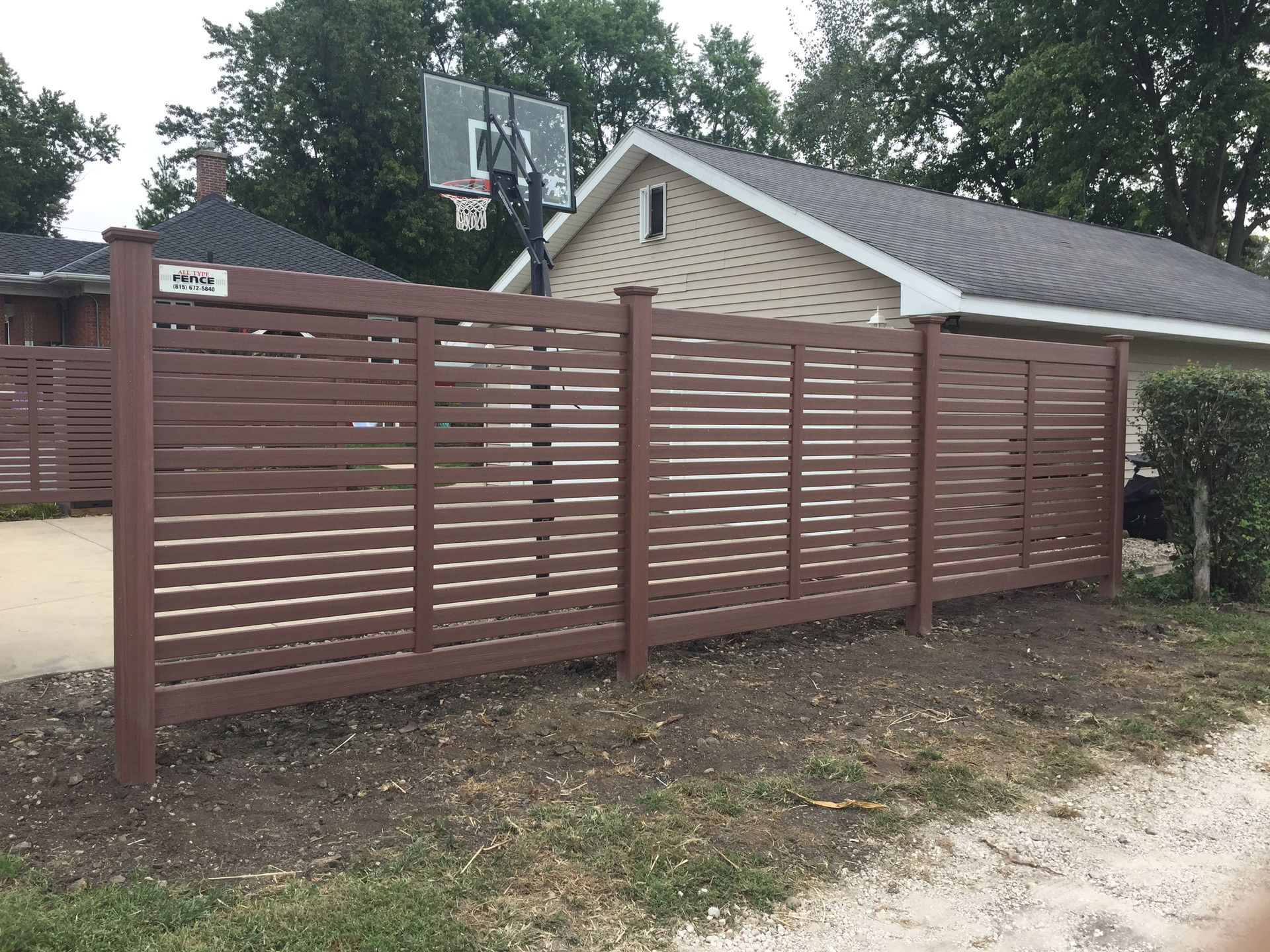 A wooden fence in front of a house with a basketball hoop in the background