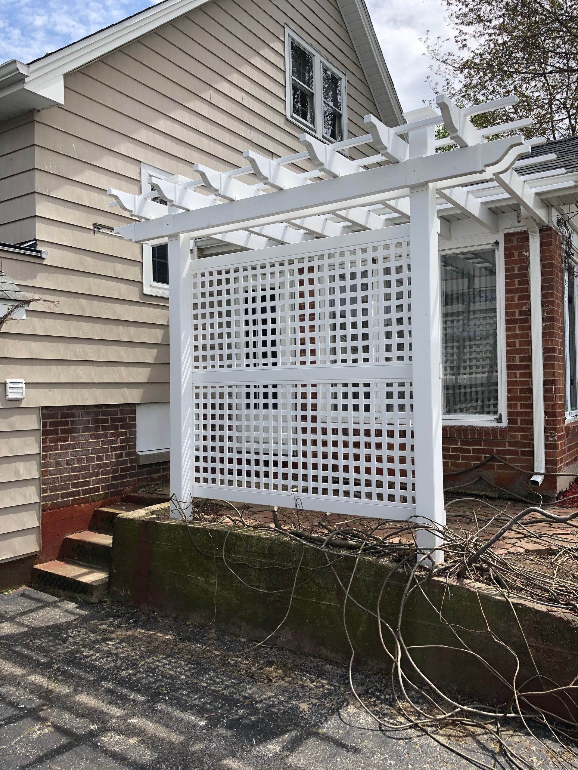 A white pergola is sitting in front of a house.