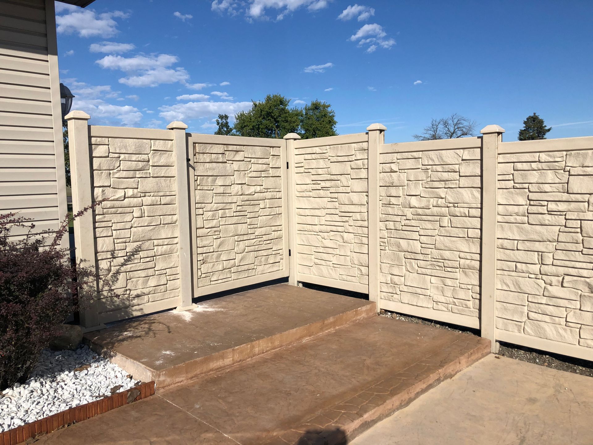 A stone fence surrounds a concrete walkway in front of a house.