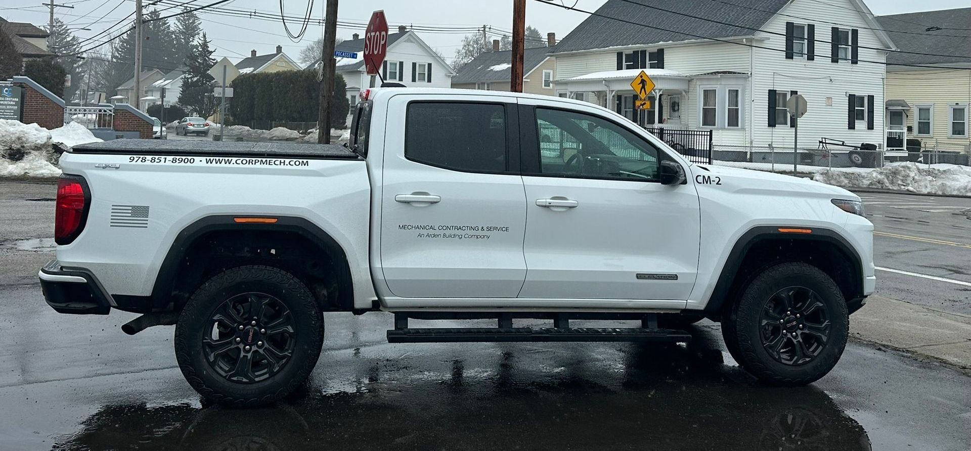 White lifted pickup truck parked on a snowy street in front of houses