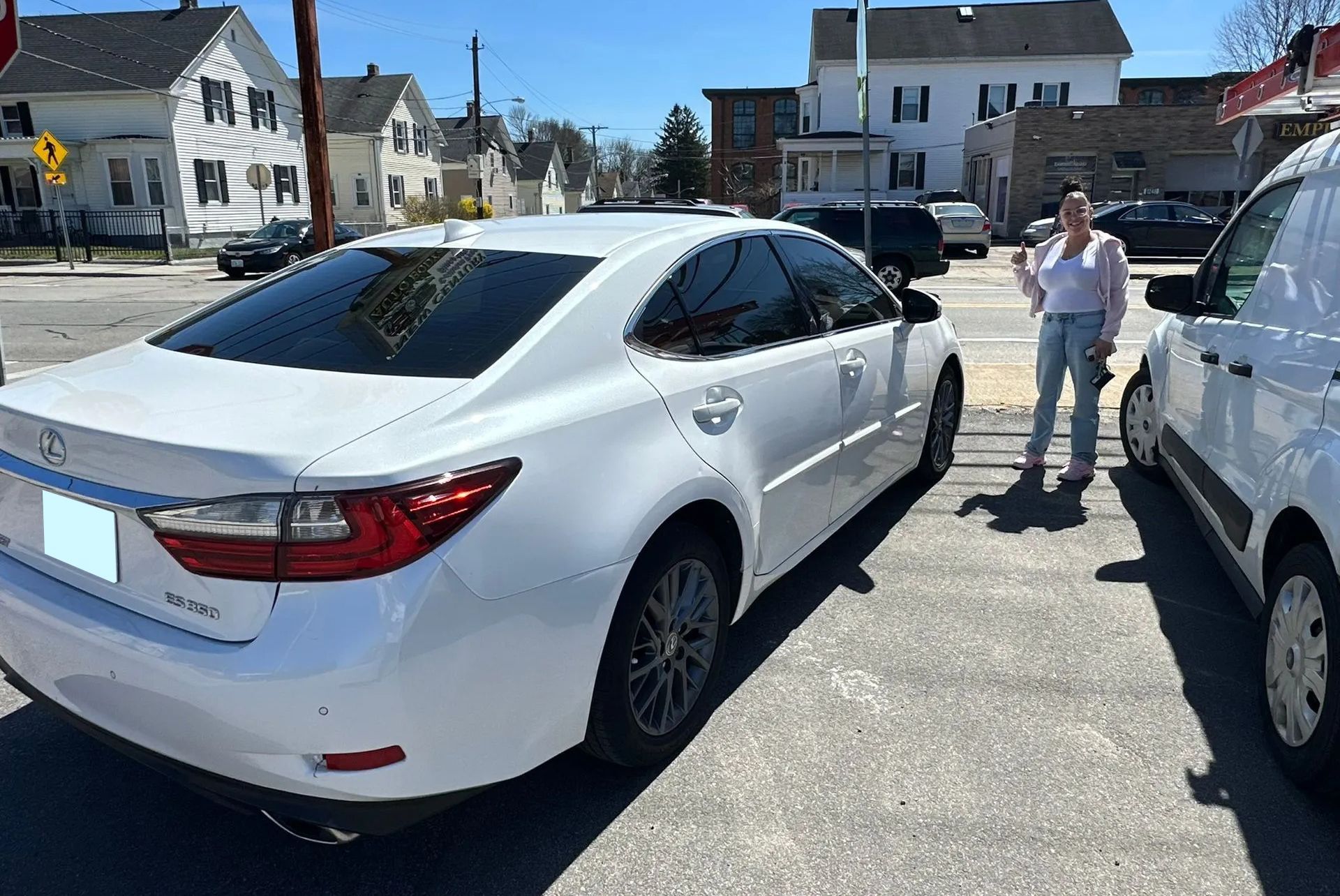 White sedan parked in a lot, with a person standing nearby on a sunny day.