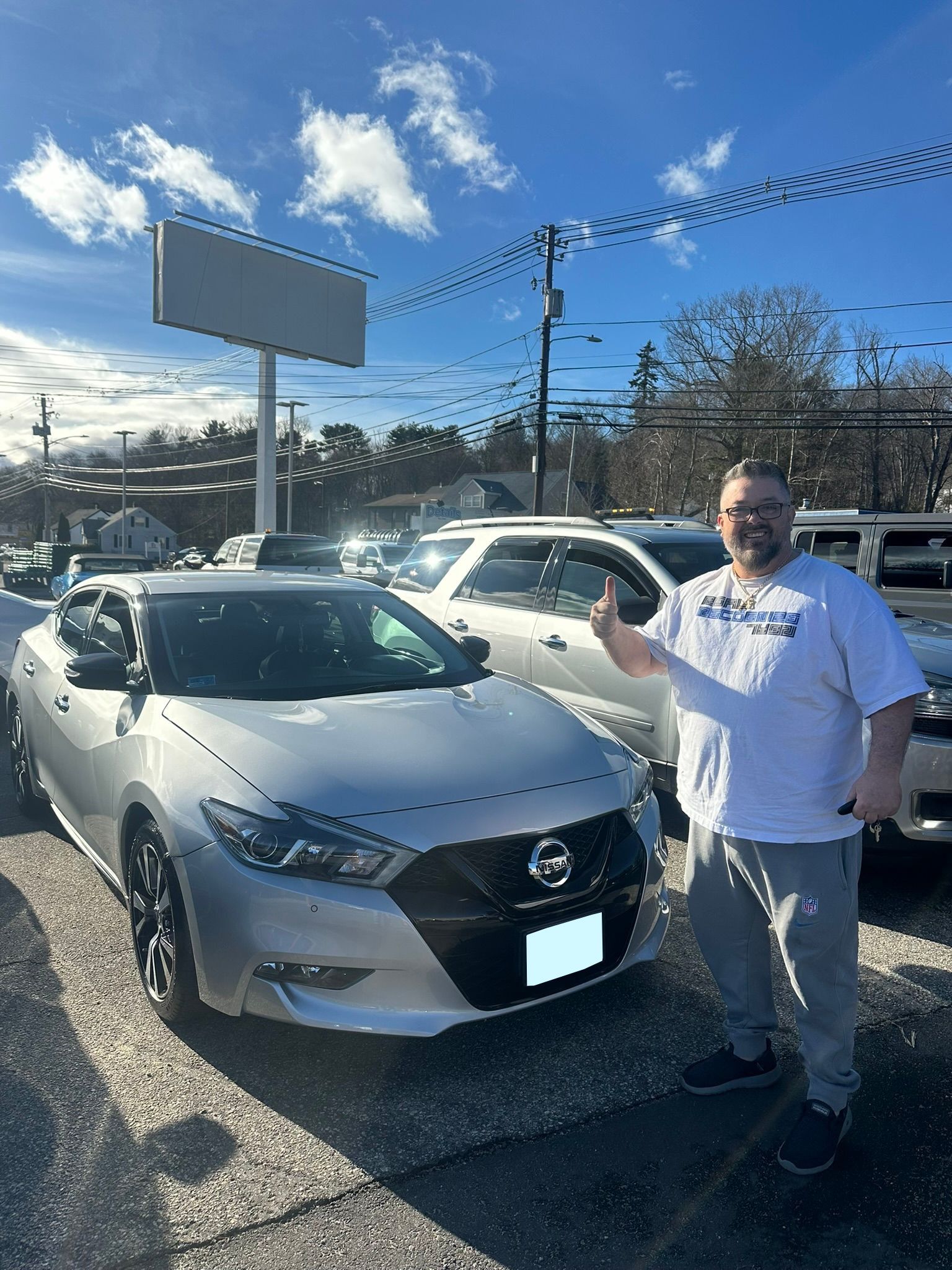 Man standing beside a silver car on a sunny car lot, pointing toward the vehicle.