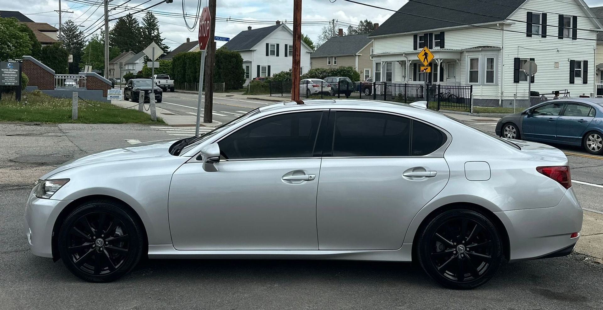 Silver sedan parked on a wet street in a residential neighborhood, with black wheels and tinted windows.