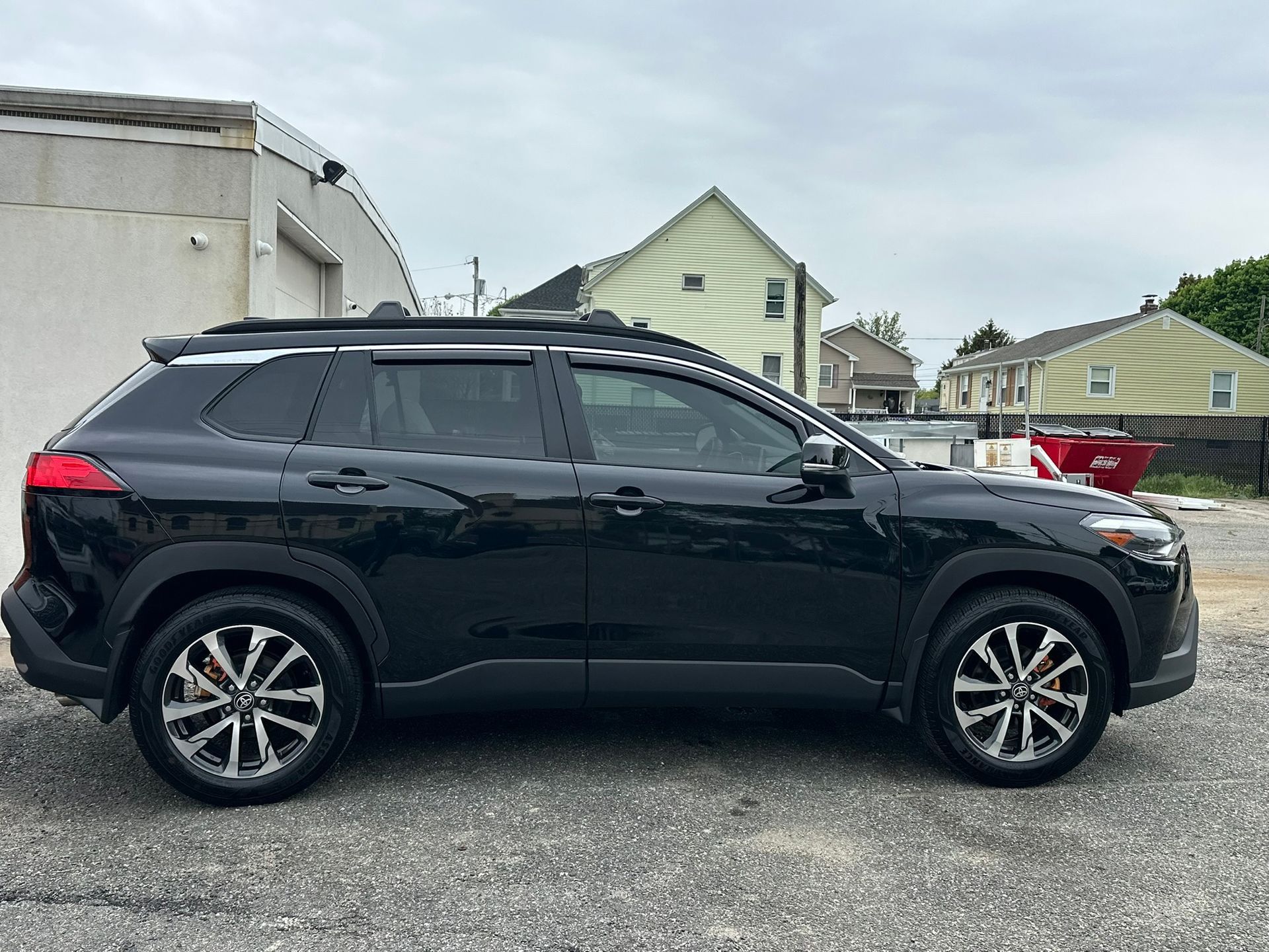 Black SUV parked in a gravel lot with houses and a cloudy sky in the background