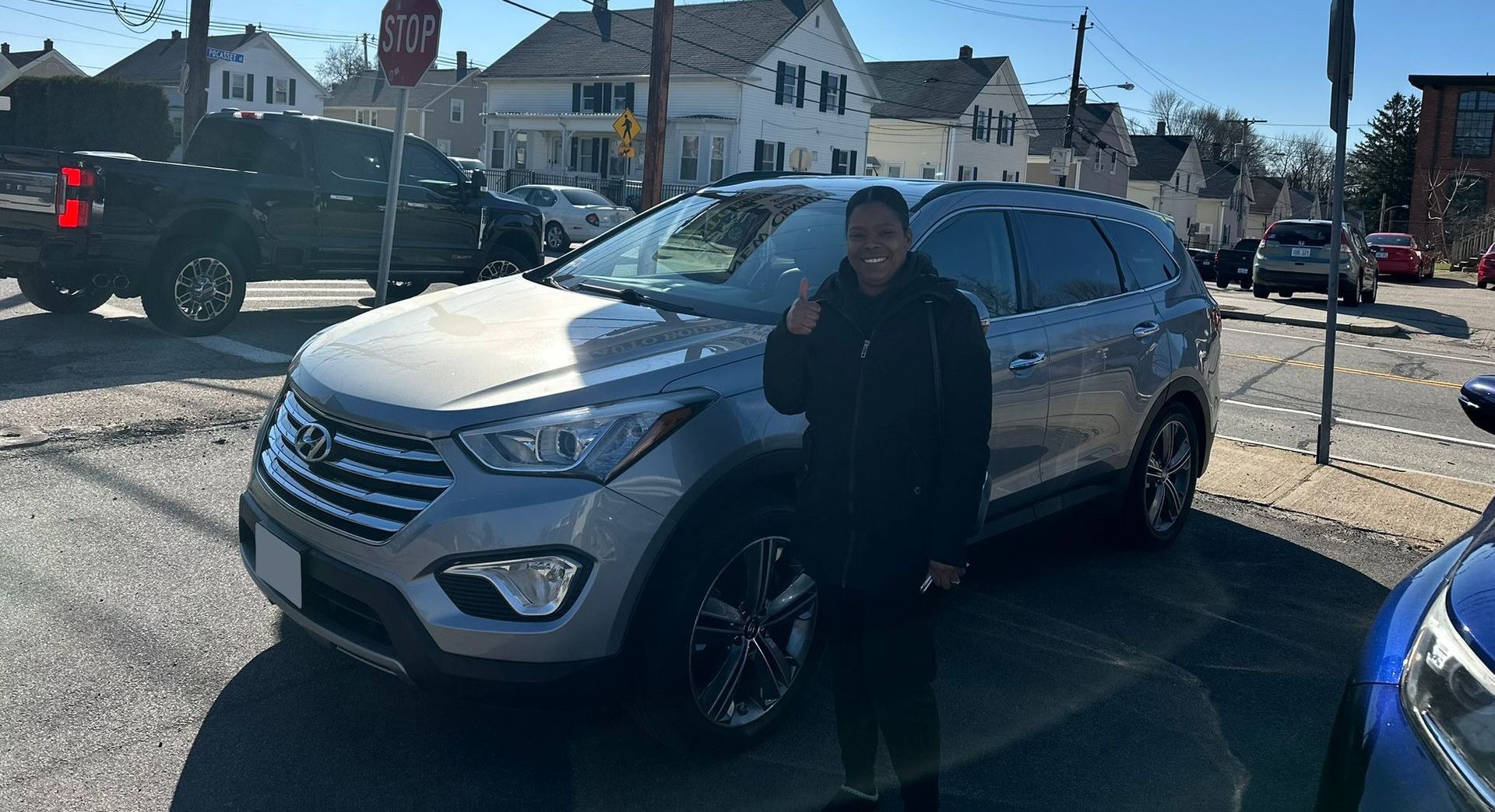 Person standing beside a silver SUV in a parking lot on a sunny day