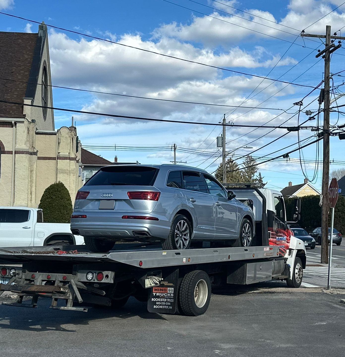 Silver SUV on a flatbed tow truck at a street intersection under a blue sky