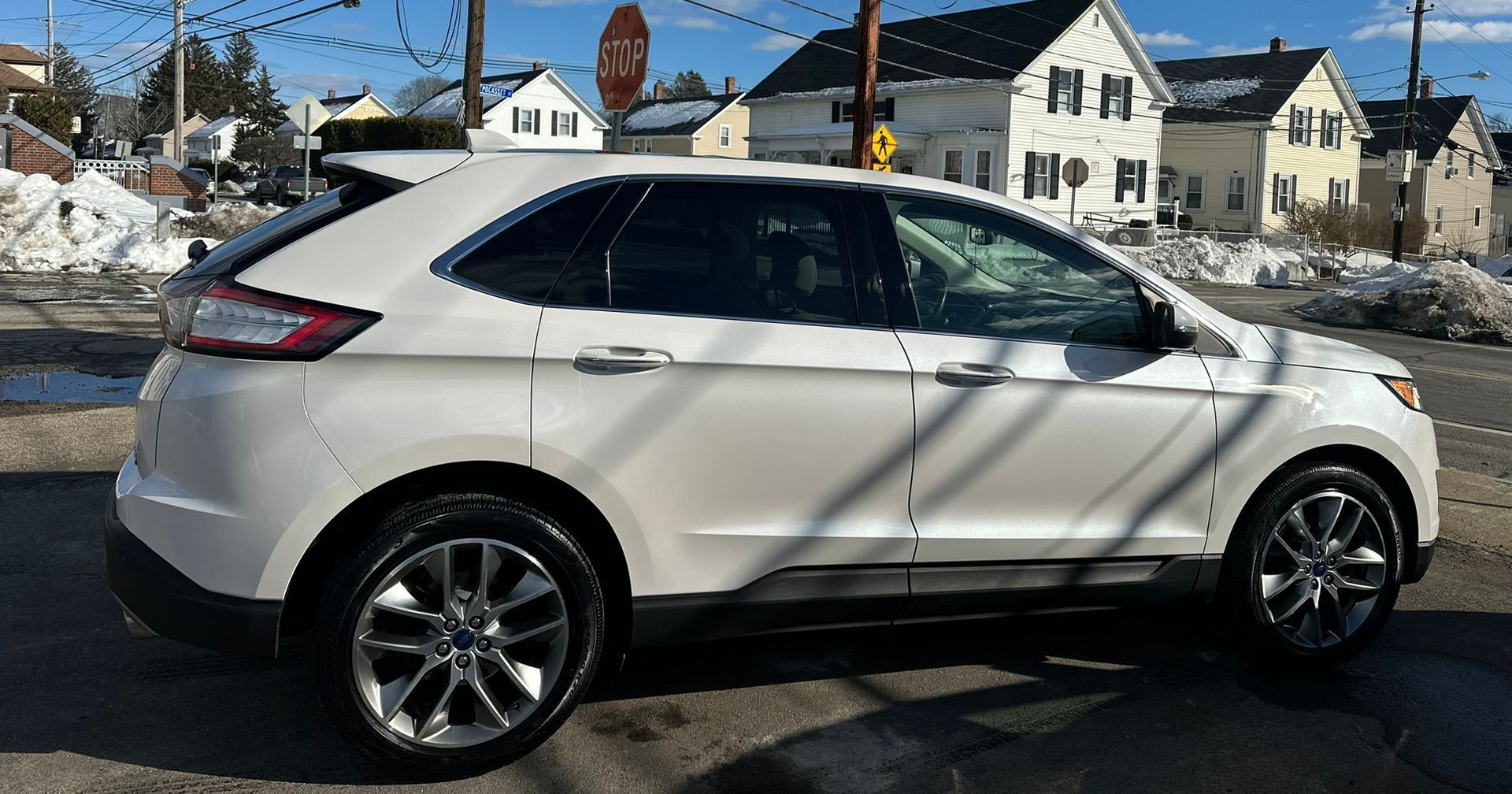 White SUV parked on a snowy residential street under clear daylight