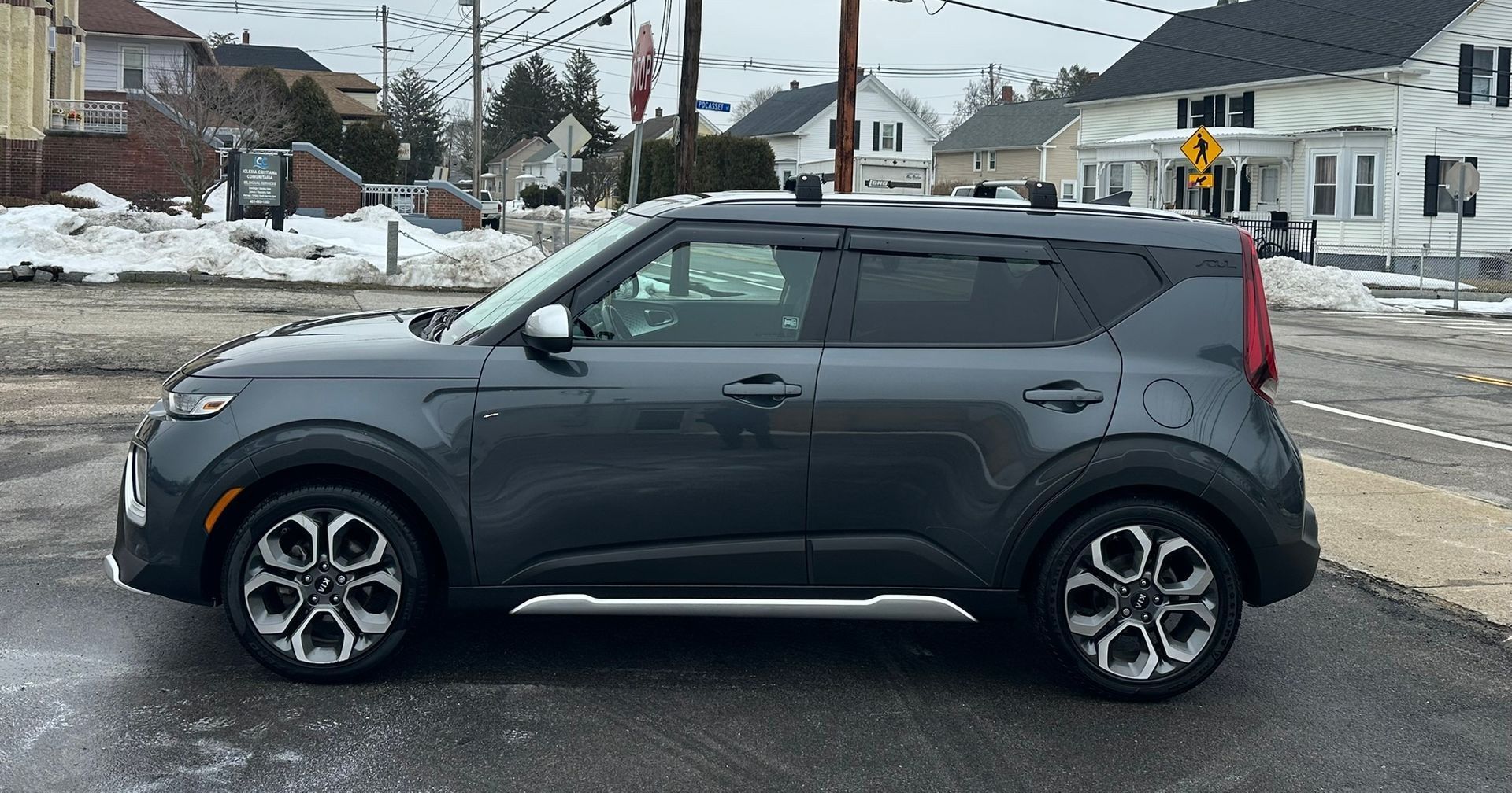 Dark gray compact SUV parked on a snowy street near a crosswalk and houses