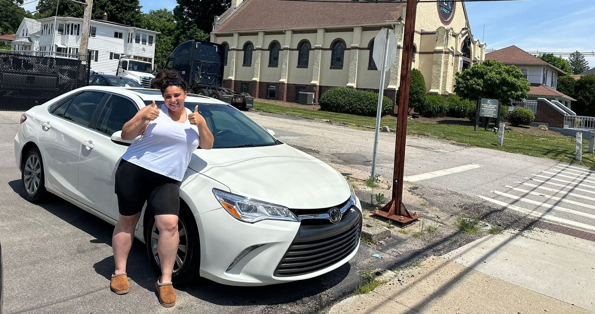 Person leaning against a white sedan on a street with historic buildings in the background