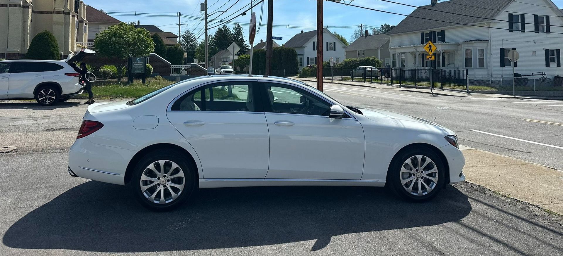 White sedan parked at a street intersection on a sunny day, with houses in the background.