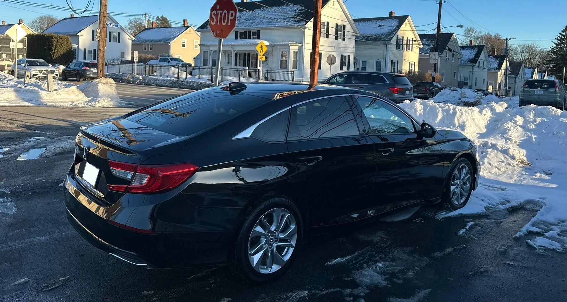 Black sedan parked on a snowy residential street near a stop sign and houses.