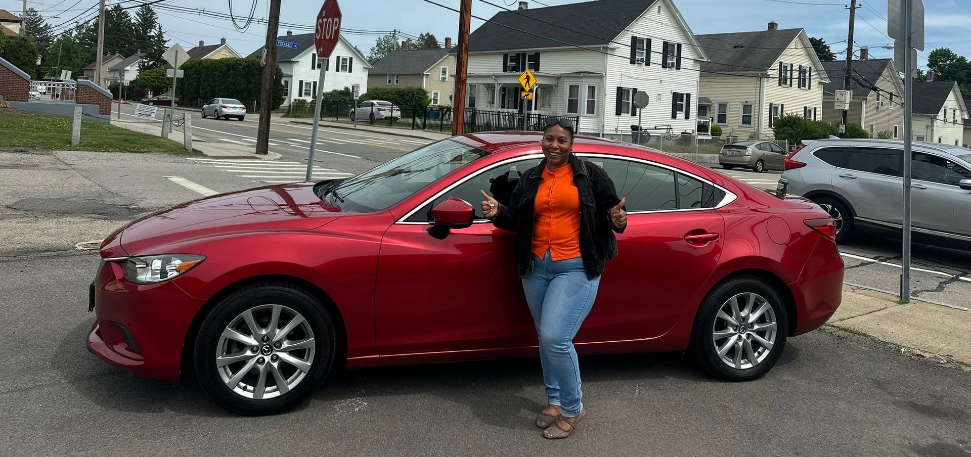Person leaning on a red sedan in a residential street with houses in the background