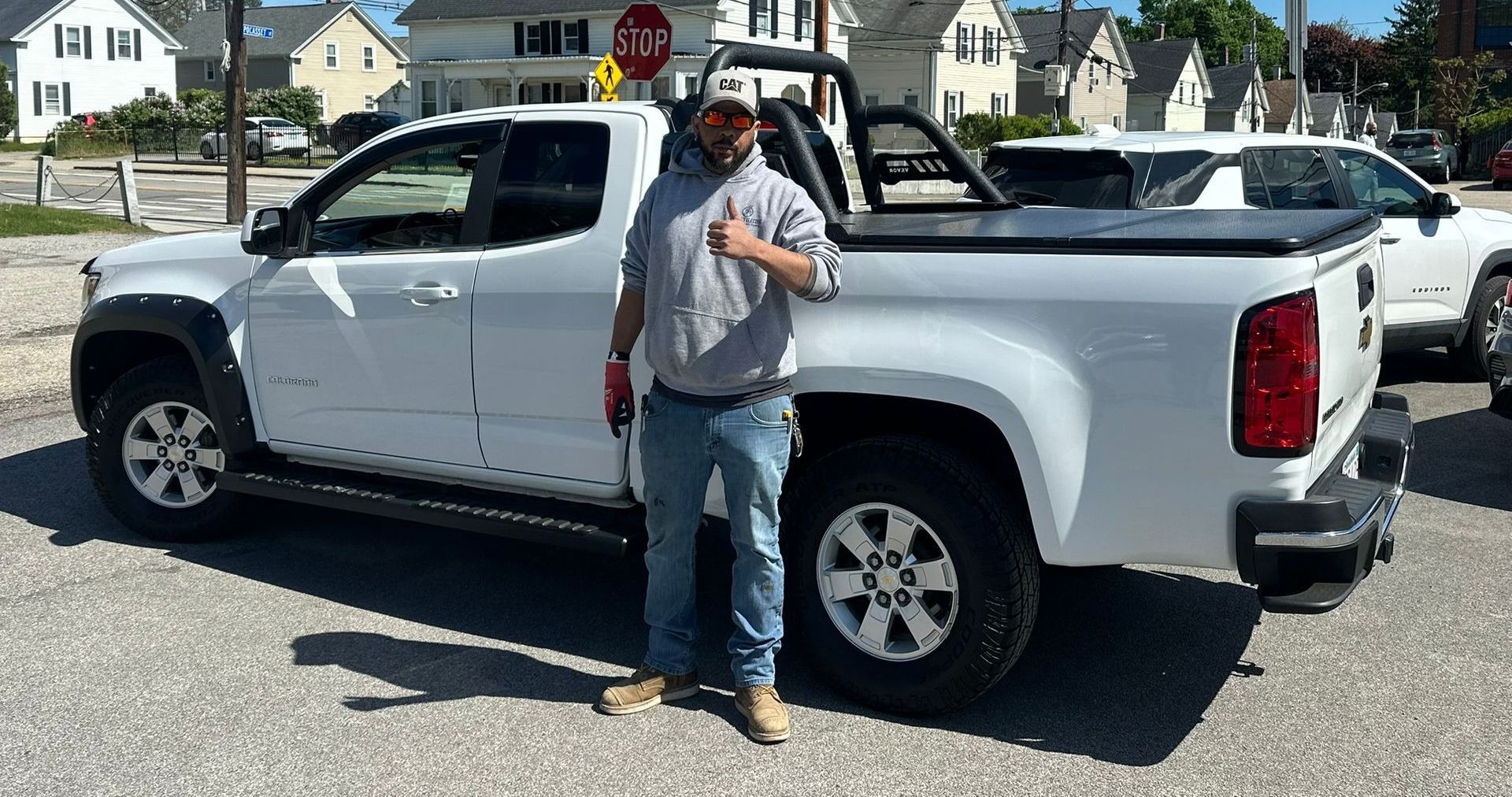 Person standing beside a white pickup truck in a suburban street, holding a bag.