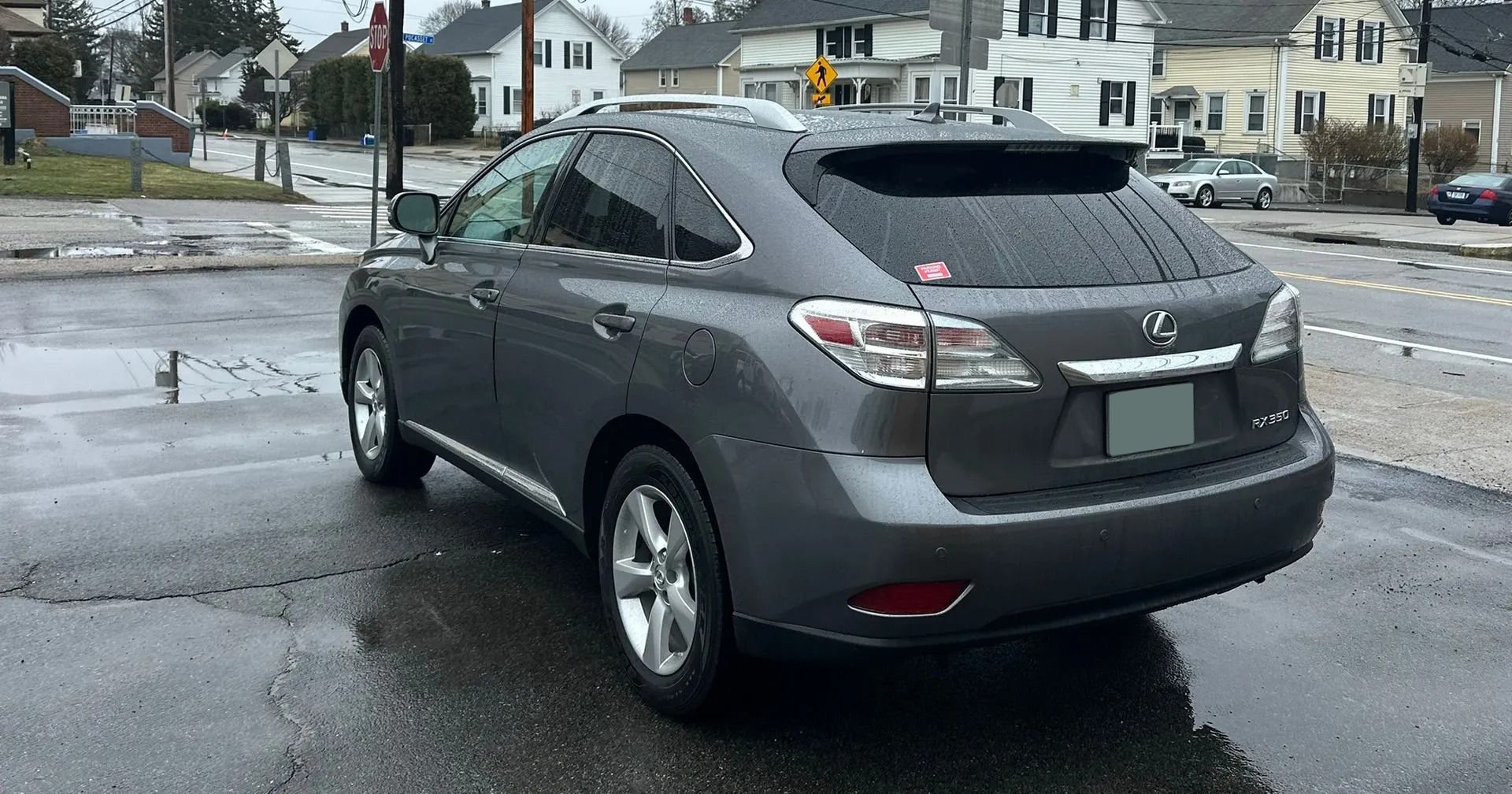 Gray sedan parked on a wet street near a crosswalk and houses on an overcast day