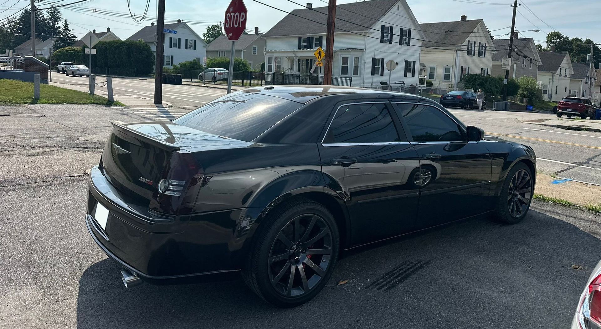 Black sedan parked on a gravel lot in front of houses on a sunny day