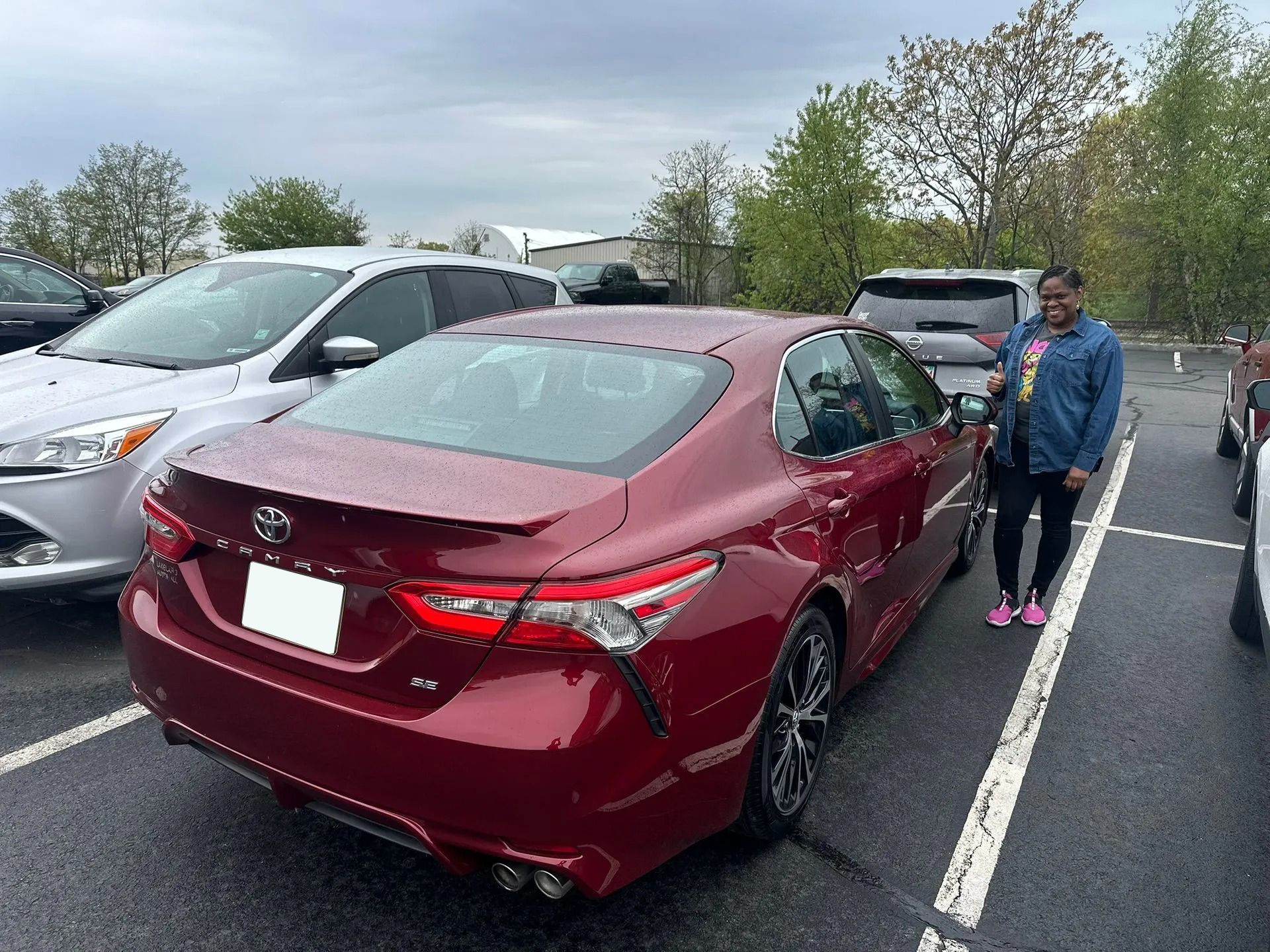 Red sedan parked in a lot beside a person in a blue jacket on a cloudy day