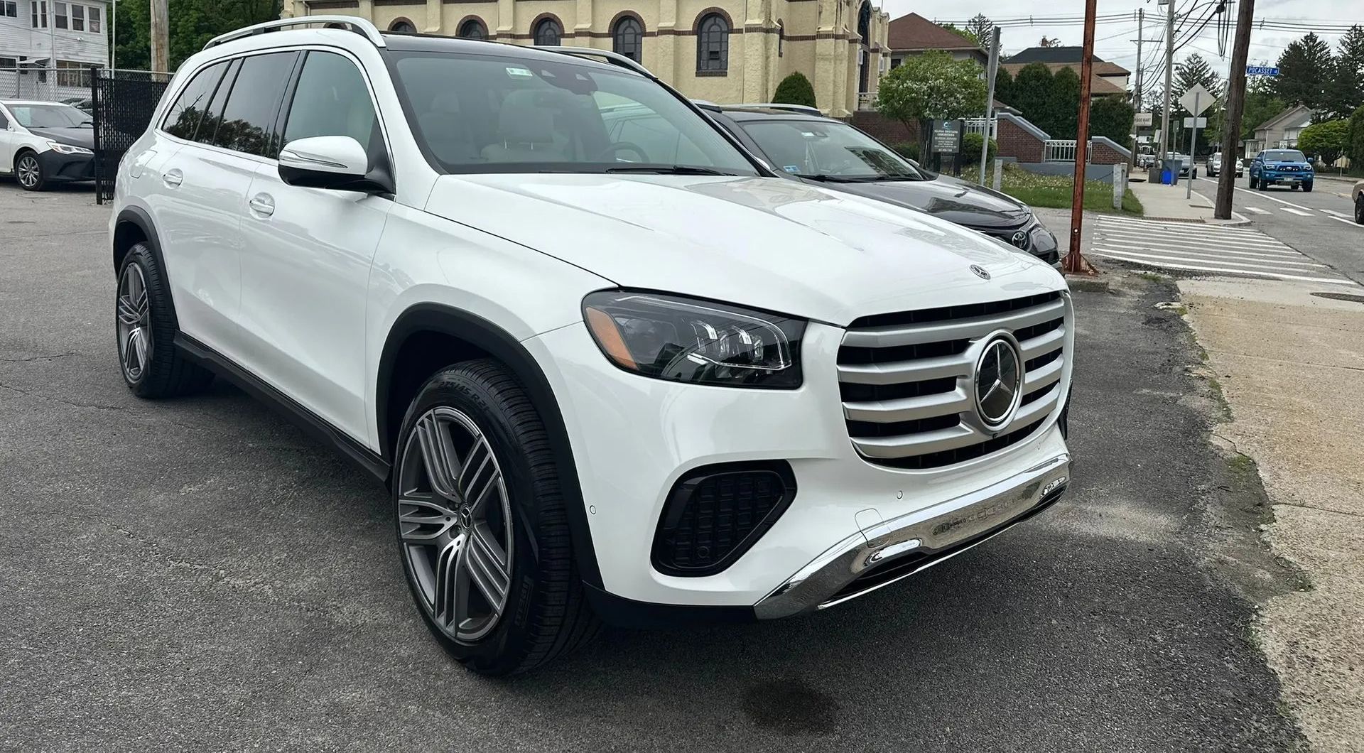 White Mercedes SUV parked on a wet street near buildings, front three-quarter view