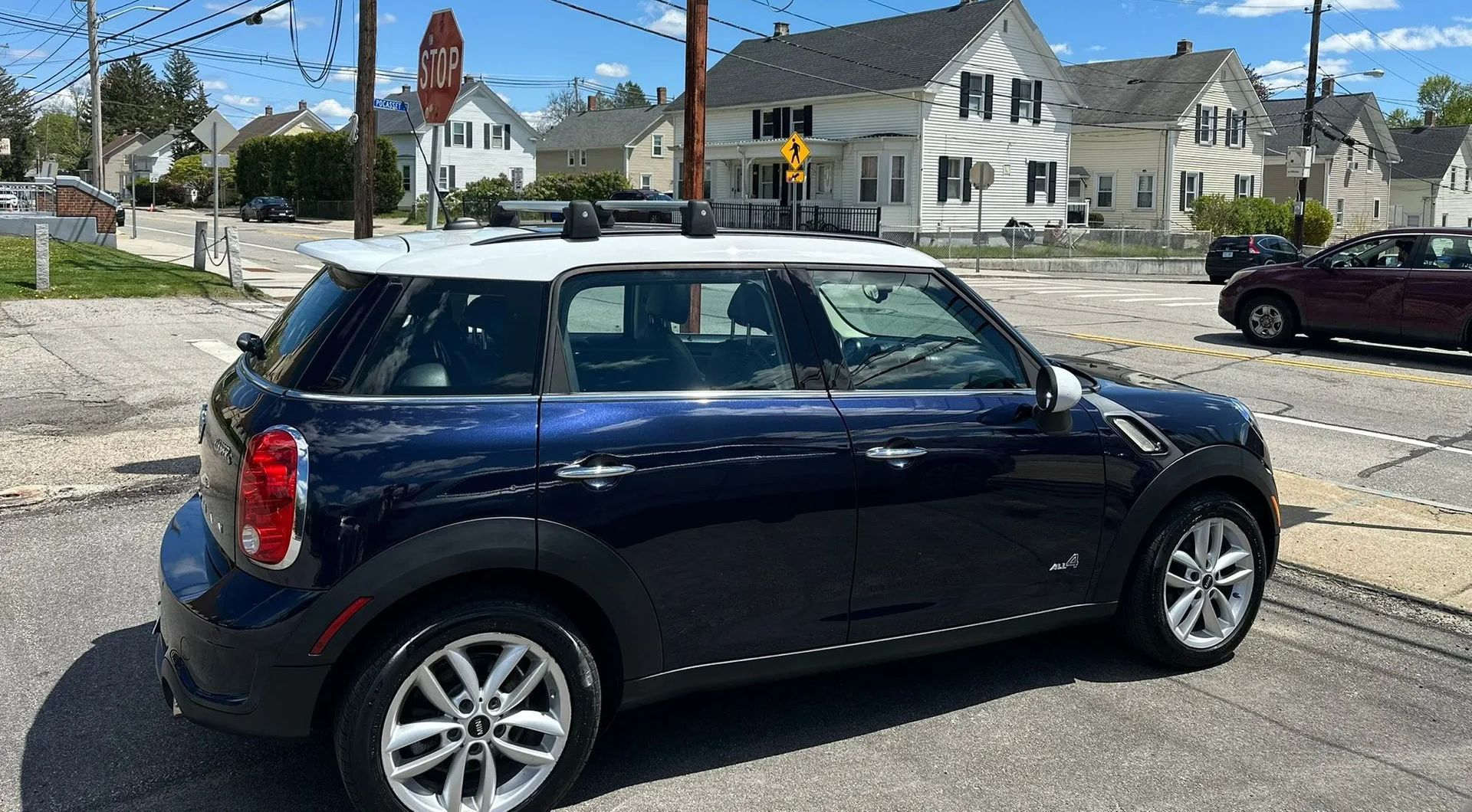Dark blue Mini Cooper parked on a street in front of houses under a clear sky.