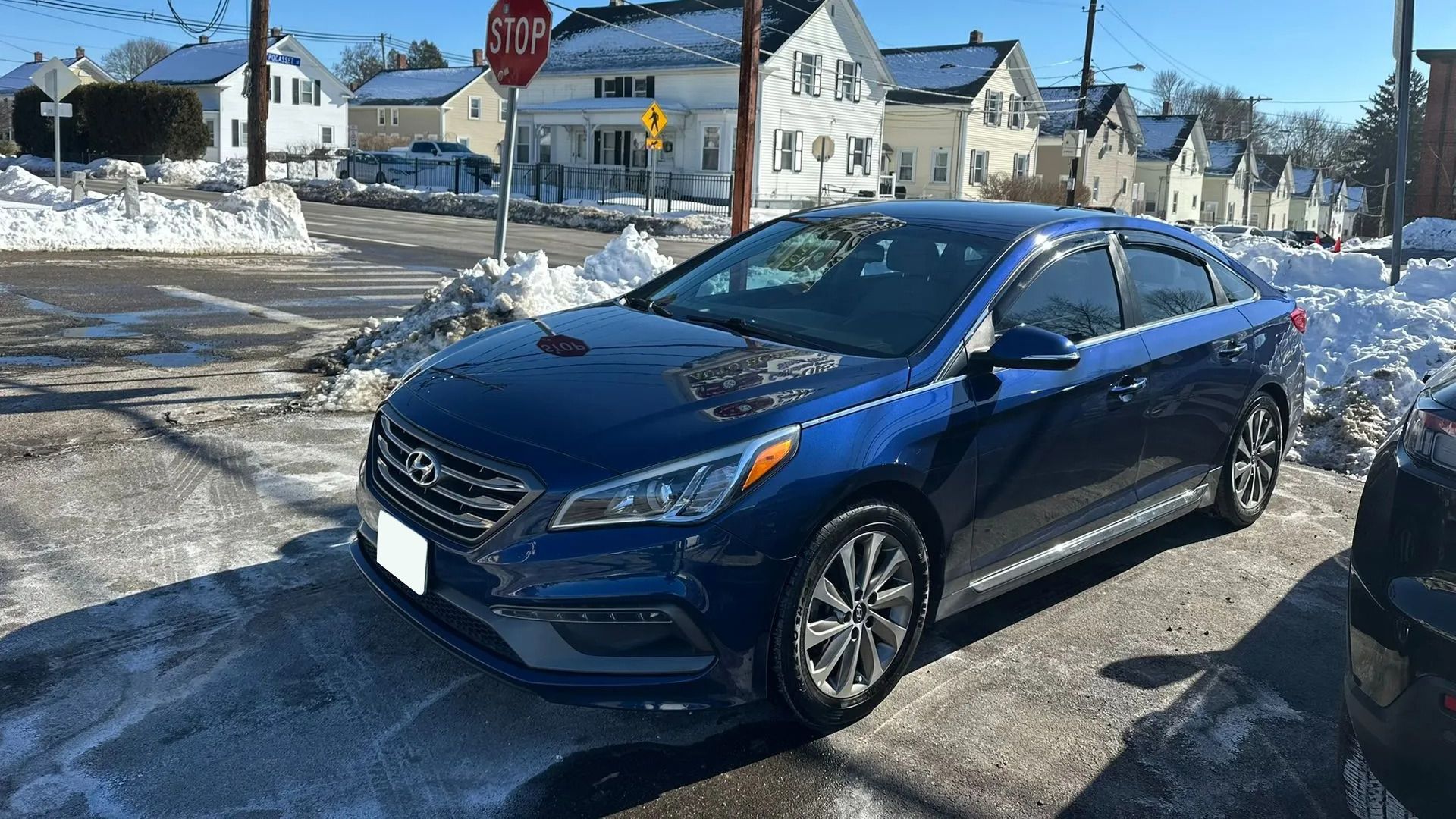 Blue sedan parked in a snowy neighborhood street under a clear sky