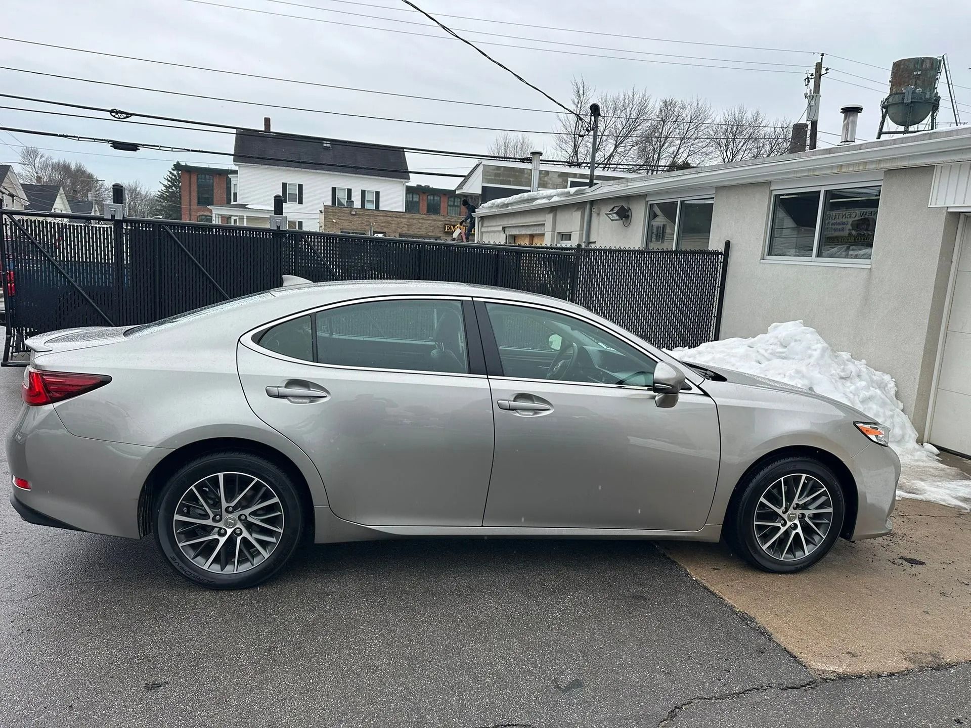 Silver sedan parked on a wet street beside a snowbank and white building